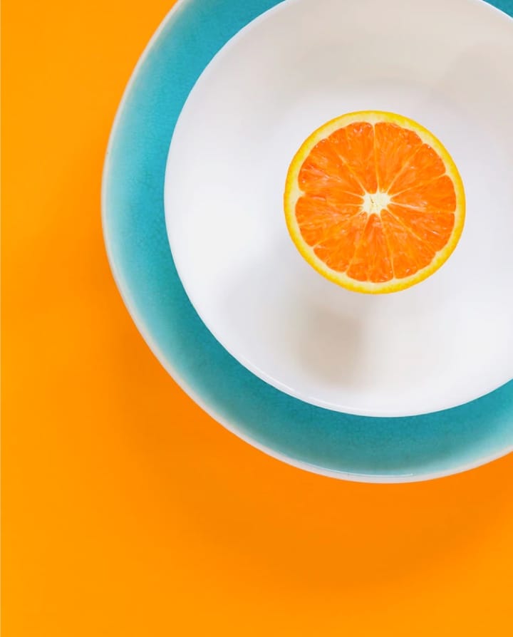 Arial view of half an orange in a blue and white bowl with an orange background