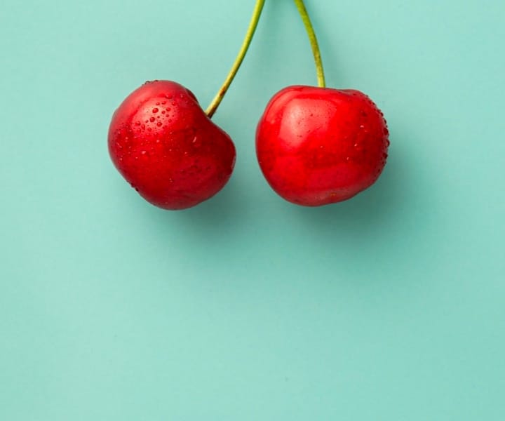 Two bright red cherries on a light green background