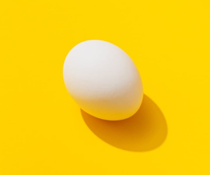 An egg on a yellow background casting a shadow